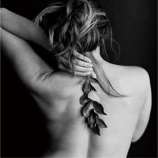 植物を片手に持ち、後ろを向く裸の女性のモノクロ画像